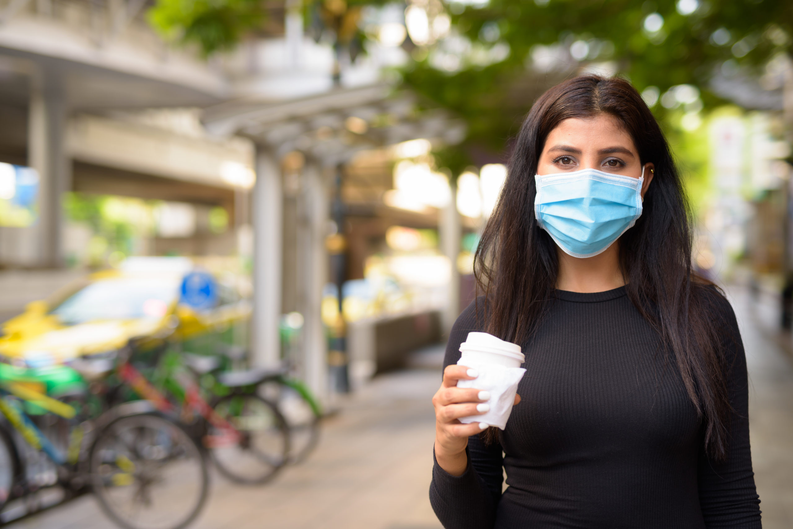 Young Indian woman with mask having coffee on the go as the new normal during covid-19 in the city
