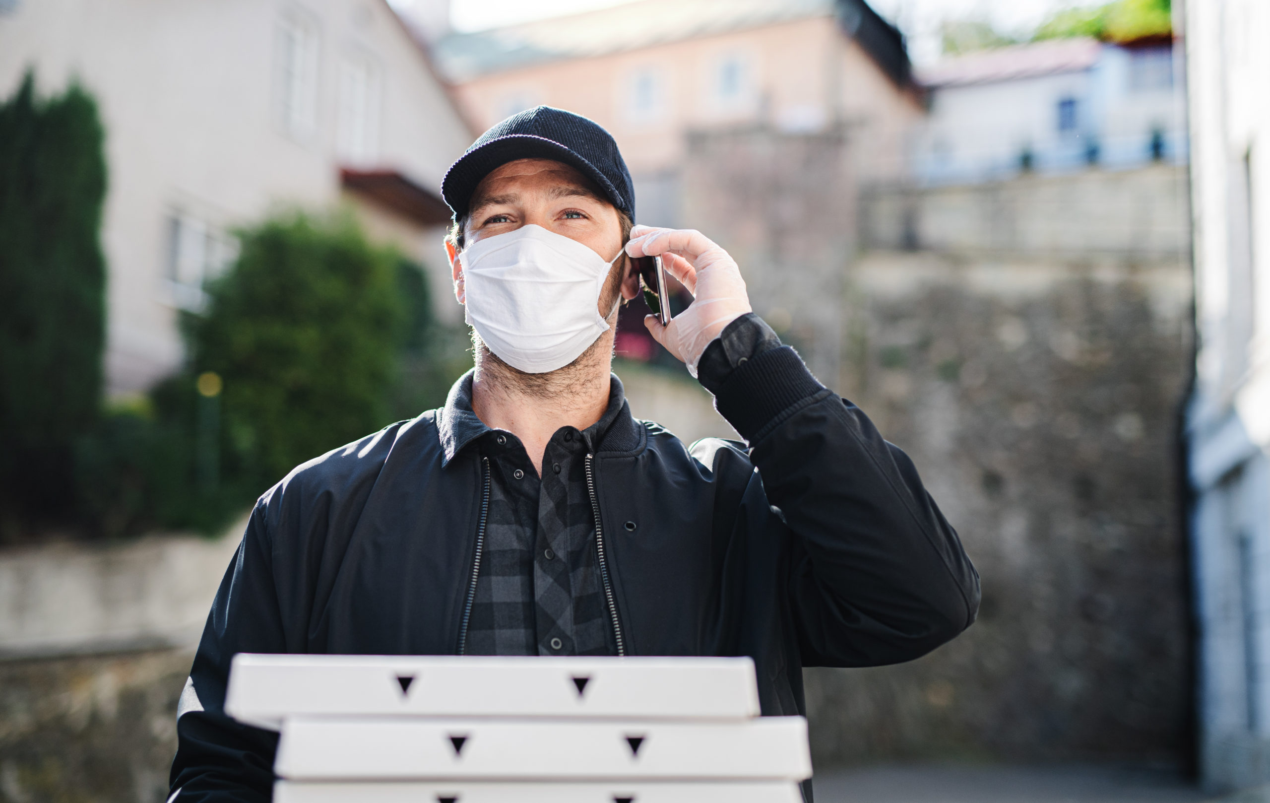 Delivery man courier with smartphone and face mask delivering pizza in town.